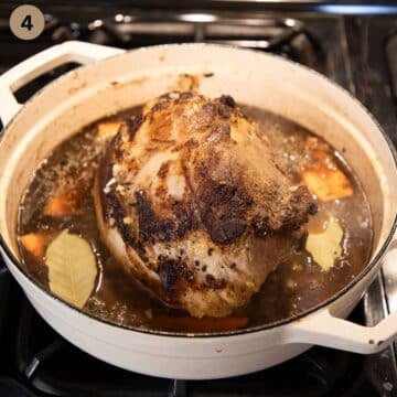 pork roast sitting in cooking liquid with bay leaves in a pot.