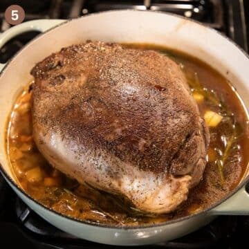 cooked venison roast in cooking liquid in a large pot.