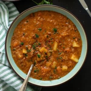 red lentil bacon soup in a bowl with a spoon in it.