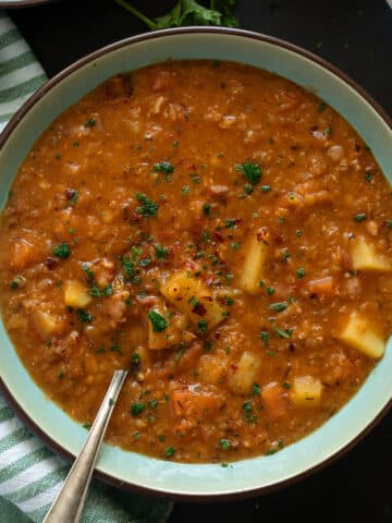 red lentil bacon soup in a bowl with a spoon in it.