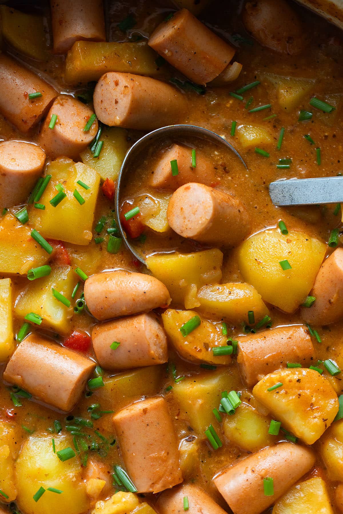 spooning goulash with potatoes and wieners using a ssmall soup ladle.