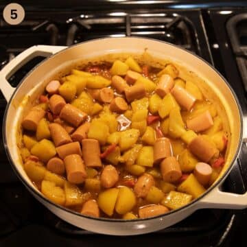 sausage pieces and potatoes simmering in stock in a pot.