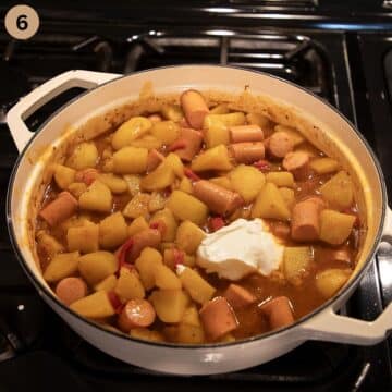 adding a dollop of sour cream to goulash with sausages and potatoes.