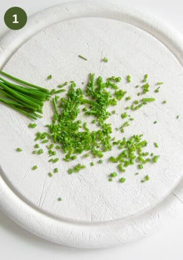 chopping chives on a round cuttting board.