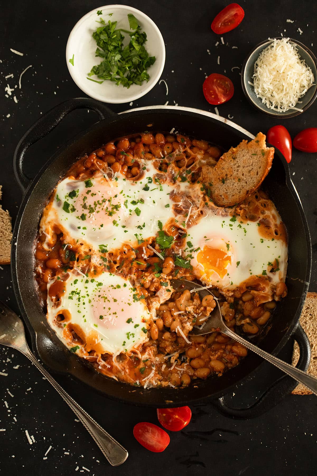 baked beans with eggs, a slice of bread and a spoon in a cast iron skillet.