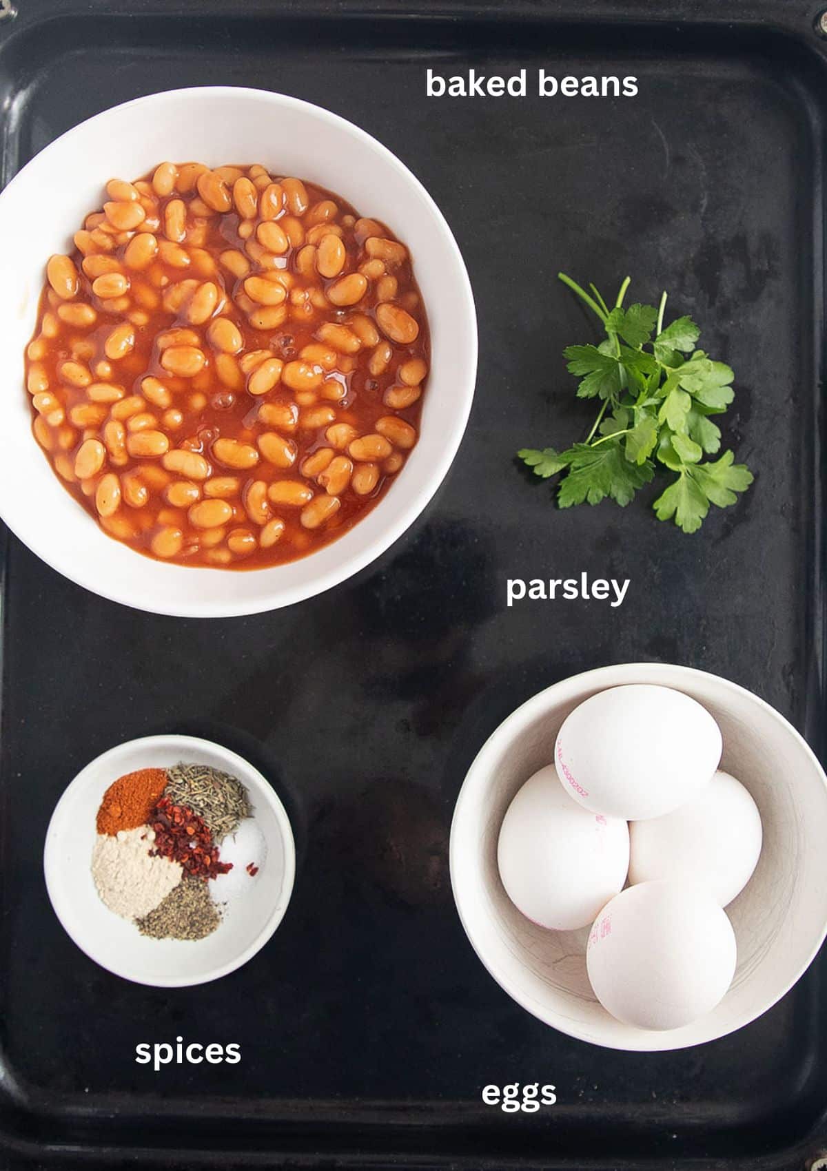 bowls with baked beans, eggs, spices and a parsley sprigs.