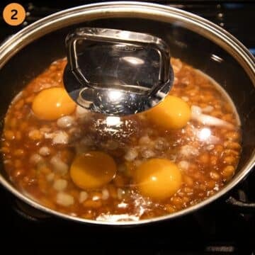 four eggs and baked beans cooking covered in a skillet.