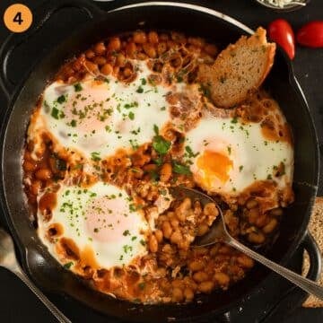 three eggs cooked on top of baked beans in a cast iron skillet.