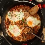 baked beans with eggs in a skillet with a slice of bread and a spoon.