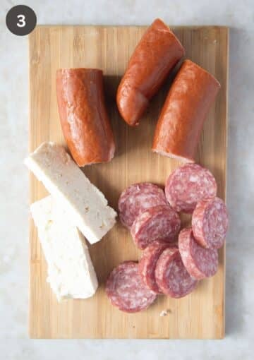 sliced feta, salami and cabanossi sausage on a wooden board.