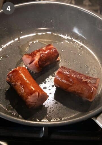 three pieces of cabanossi sausage frying in a small pan.