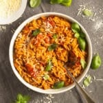 creamy tomato orzo topped with basil leaves in a bowl with a spoon in it.