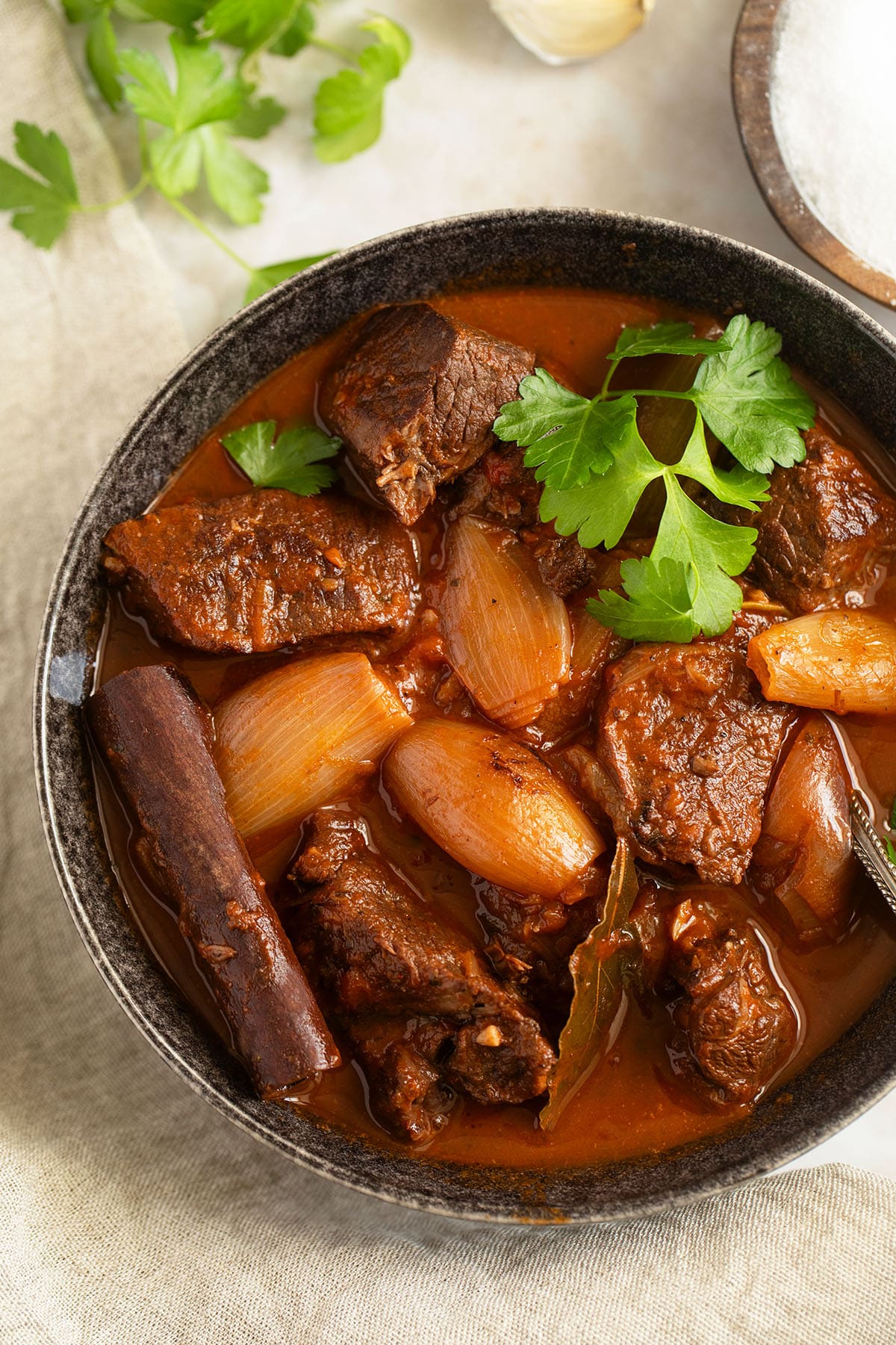 bowl of lamb stifado garnished with parsley and a cinnamon stick.