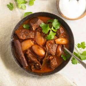 greek lamb stifado in a bowl with a spoon in it, a small bowl of salt beside it.