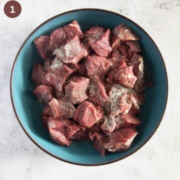 chunks of raw lamb shoulder seasoned with salt, pepper and garlic in a bowl.