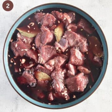 lamb pieces marinating in red wine and vinegar in a large bowl.