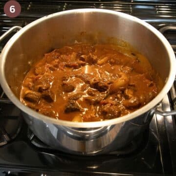cooked lamb stifado in a large heavy-bottomed pot on the stove top.