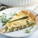 one slice of asparagus and salmon quiche on a small plate with some herbs.