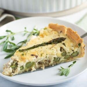 one slice of asparagus and salmon quiche on a small plate with some herbs.