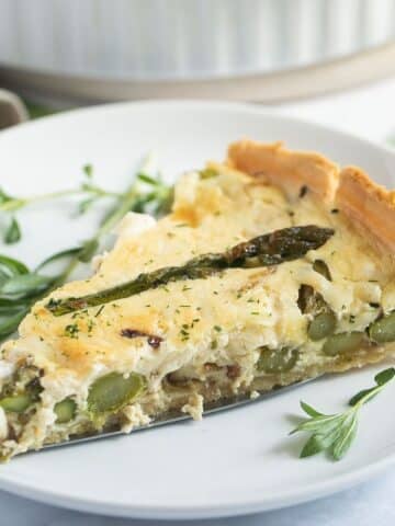 one slice of asparagus and salmon quiche on a small plate with some herbs.