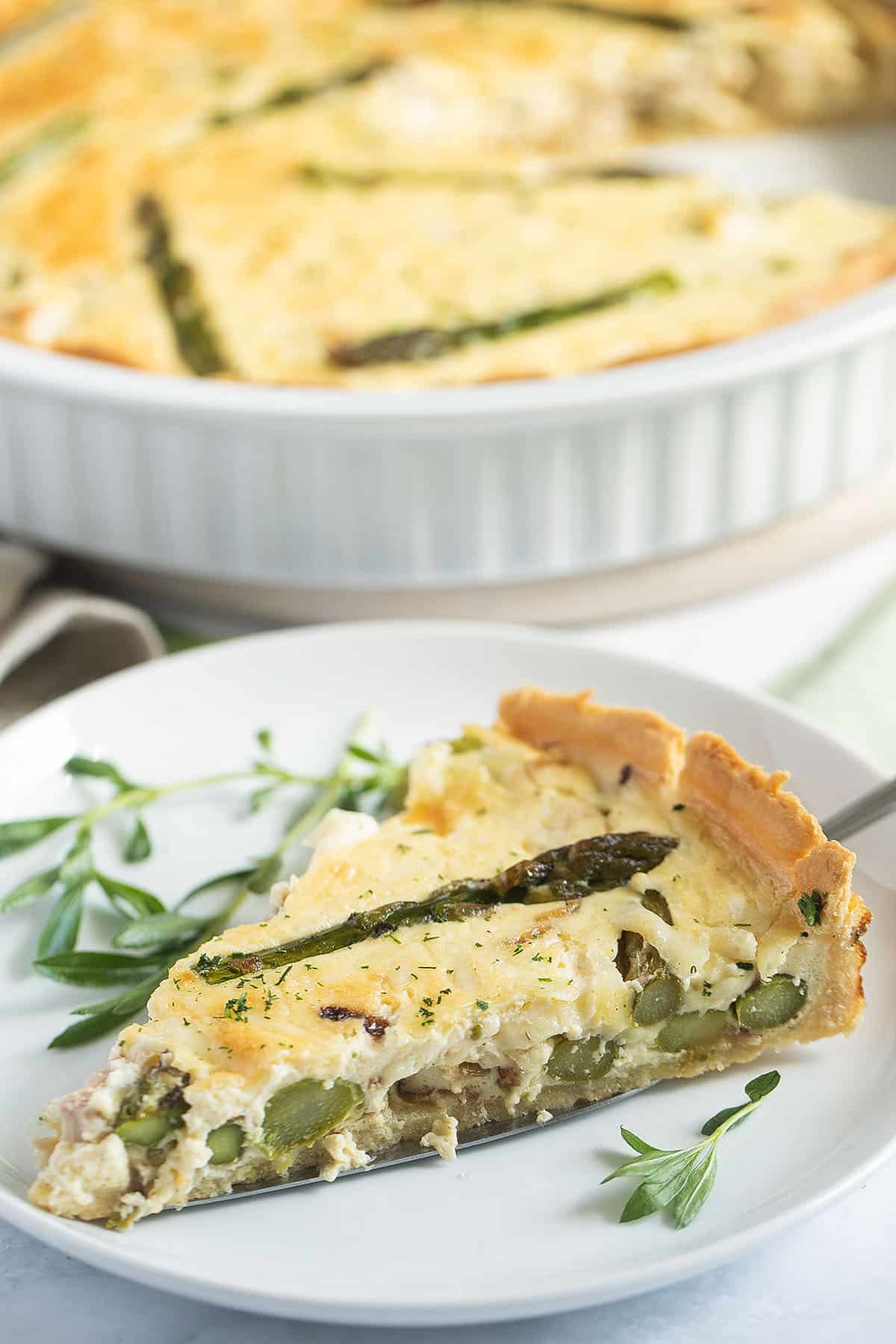 one slice of salmon and asparagus quiche on a plate, the rest of the quiche behind it.