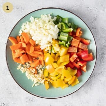 chopped colorful peppers, onions, garlic and carrots on a plate.