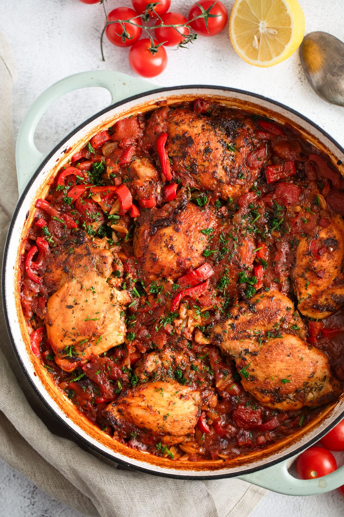 baked chicken and orzo in a pot, small tomatoes and a lemon half on the side.