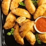many golden ham and cheese empanadas and a small bowl of salsa.