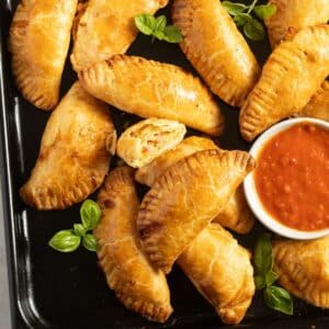 many golden ham and cheese empanadas and a small bowl of salsa.