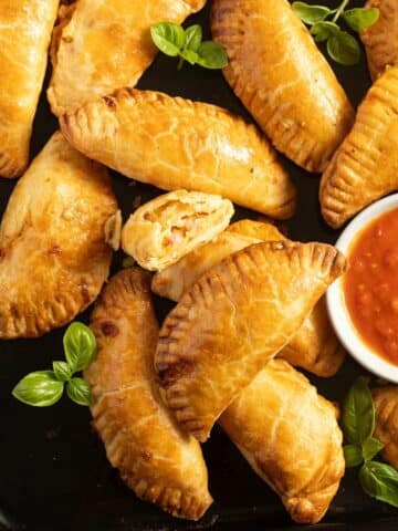 many golden ham and cheese empanadas and a small bowl of salsa.