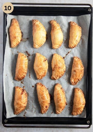 baked empanadas arranged on a baking tray lined with parchment paper.