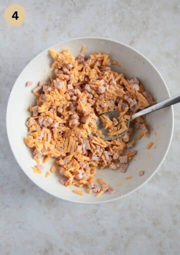 mixing ham and cheese filling for empanadas in a bowl with a spoon.