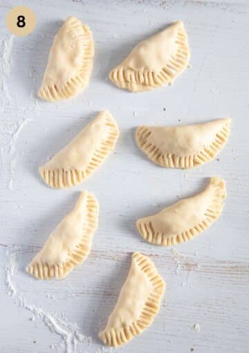 unbaked, crimped empanadas on the working surface.