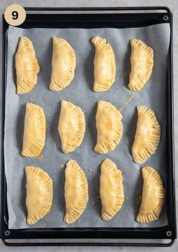 unbaked empanadas arranged on a baking sheet.