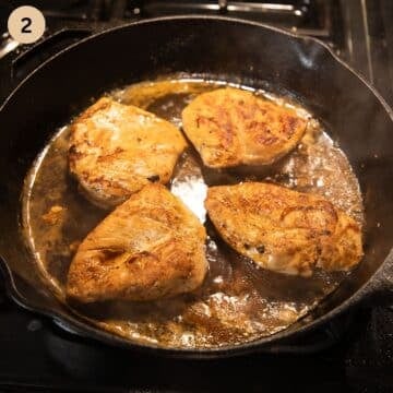 four chicken breasts cooking in white wine in a skillet.