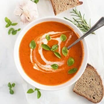 roasted garlic and tomato soup topped with cream and basil leaves in a bowl.