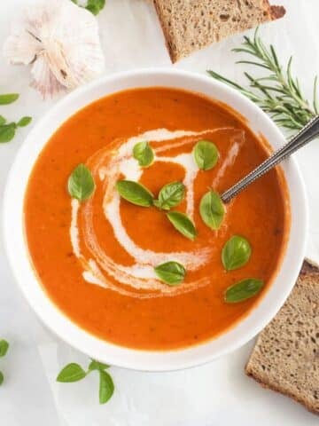 roasted garlic and tomato soup topped with cream and basil leaves in a bowl.
