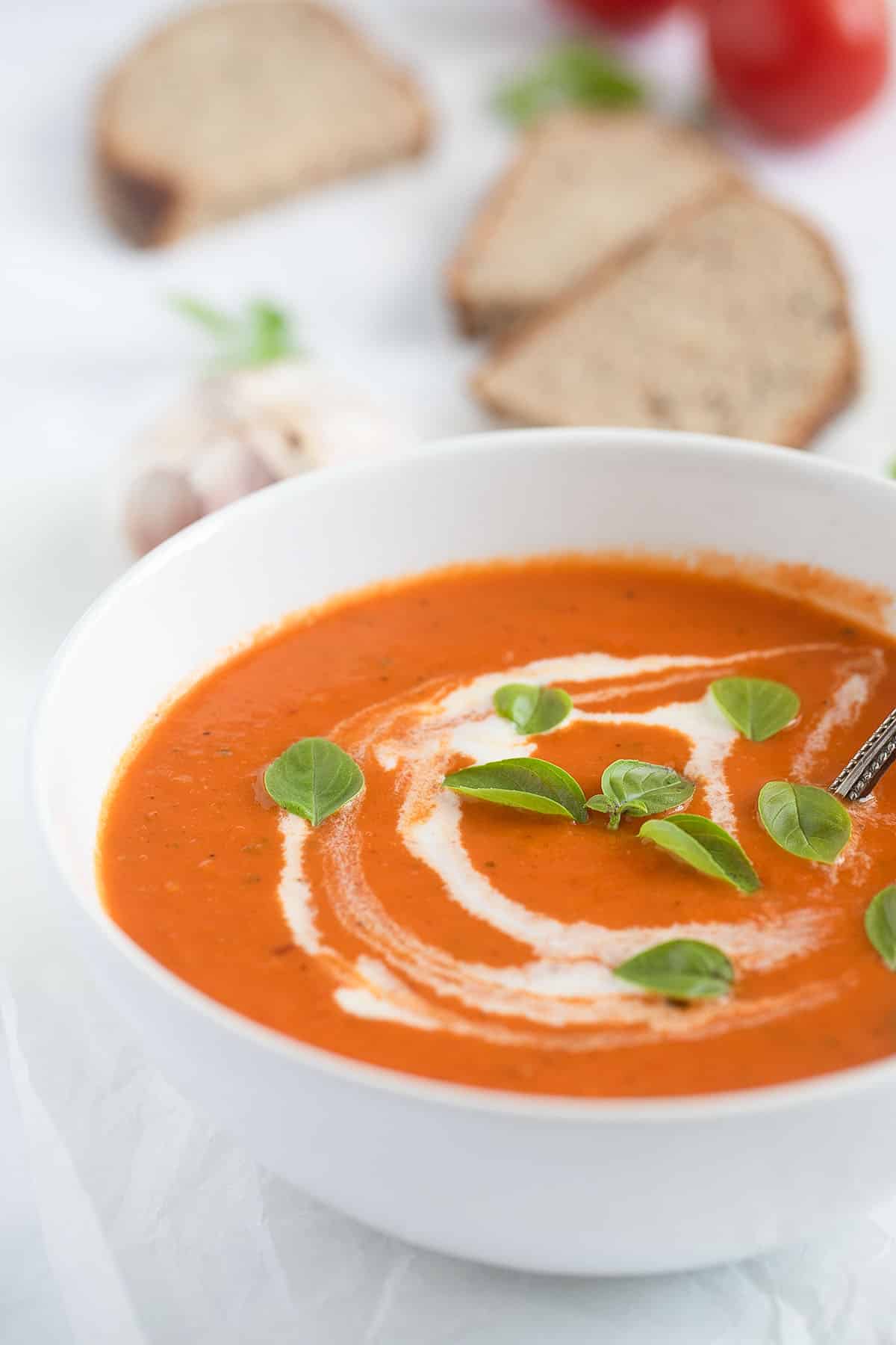 a bowl of roasted garlic and tomato soup sprinkled with cream and basil leaves.