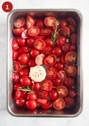 halved tomatoes and a bulb of garlic in a roasting pan before roasting.