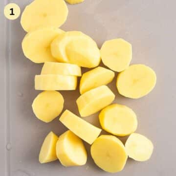 thickly sliced raw potatoes on a cutting board.