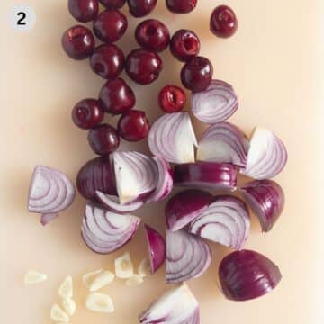 pitted cherries, thickly sliced red onions and thinly sliced garlic cloves on a cutting board.