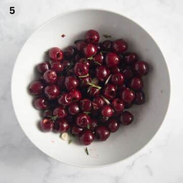 pitted cherries mixed with olive oil, garlic and herbs in a large bowl.