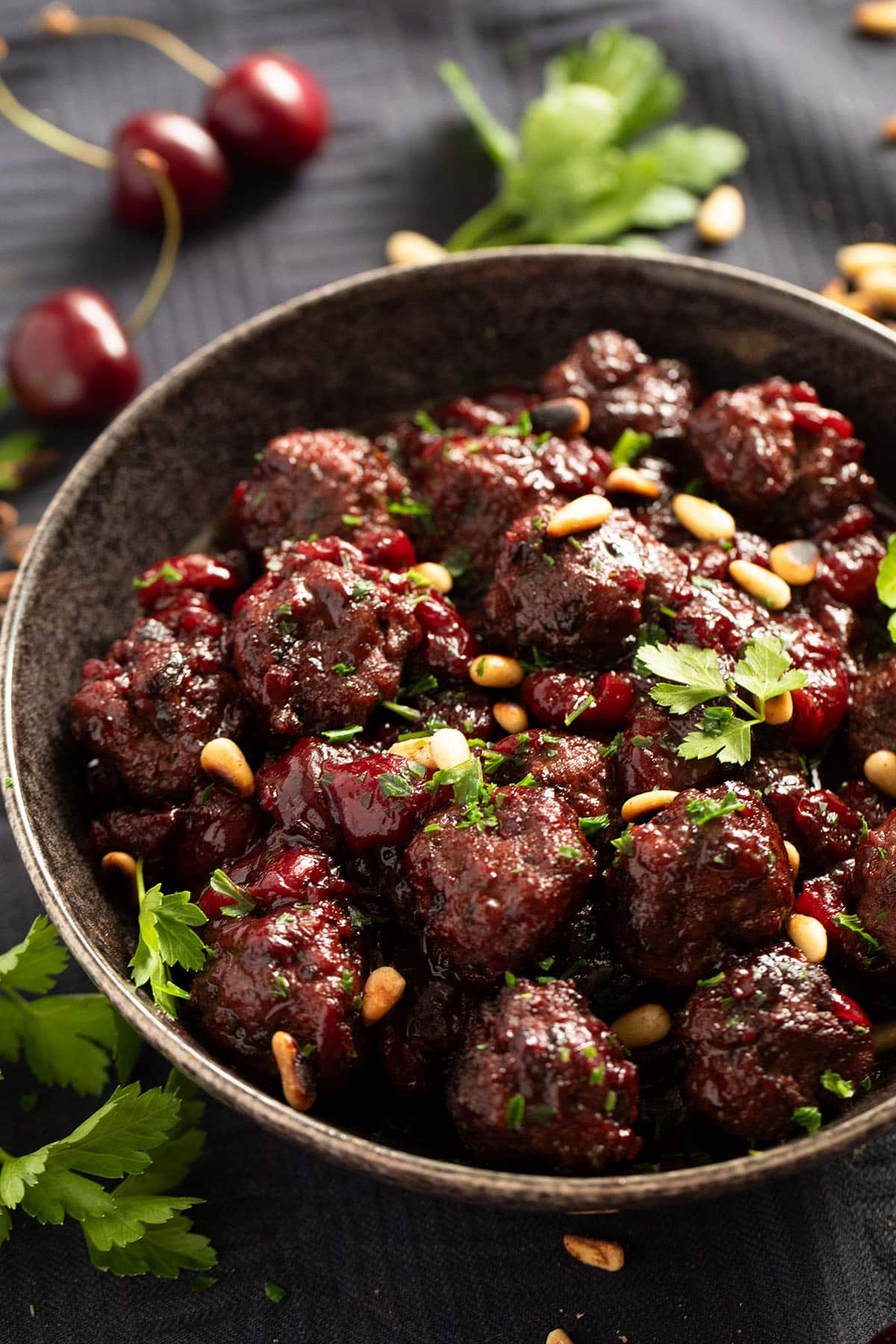 small meatballs covered in cherry sauce in a bowl, parsley and cherries around it.
