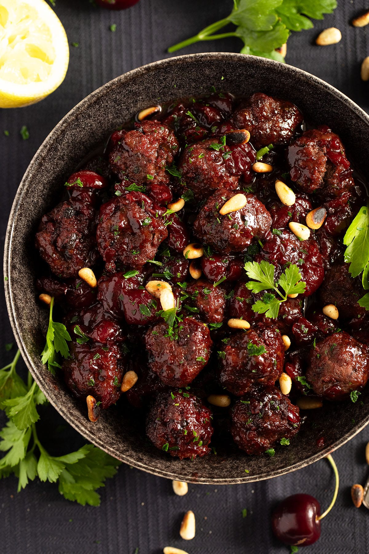 meatballs cooked in cherry sauce and sprinkled with pine nuts and parsley.