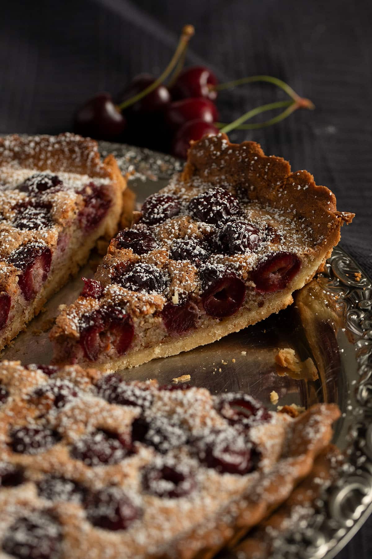 a slice of cherry tart showing the cherries inside cut from the whole tart.