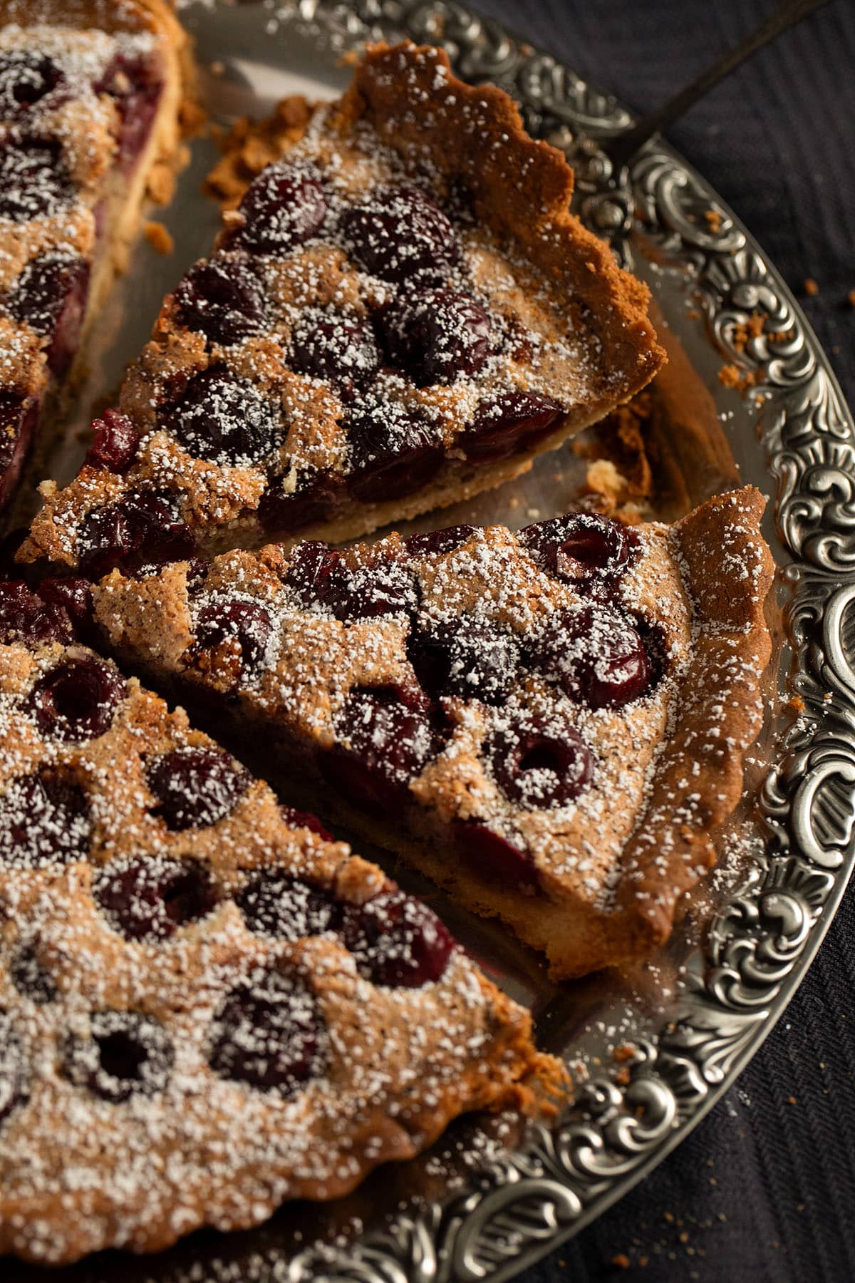 cherry tart sprinkled with confectioner's sugar and sliced on a serving platter.