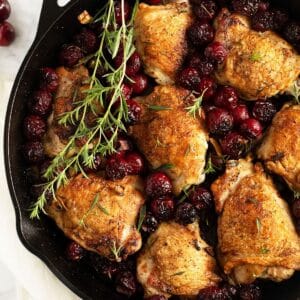 chicken with cherries and a few sprigs of thyme in a cast iron skillet.