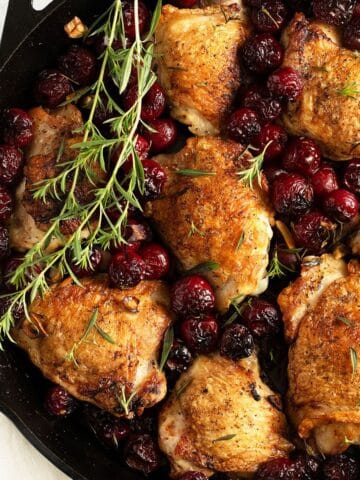 chicken with cherries and a few sprigs of thyme in a cast iron skillet.