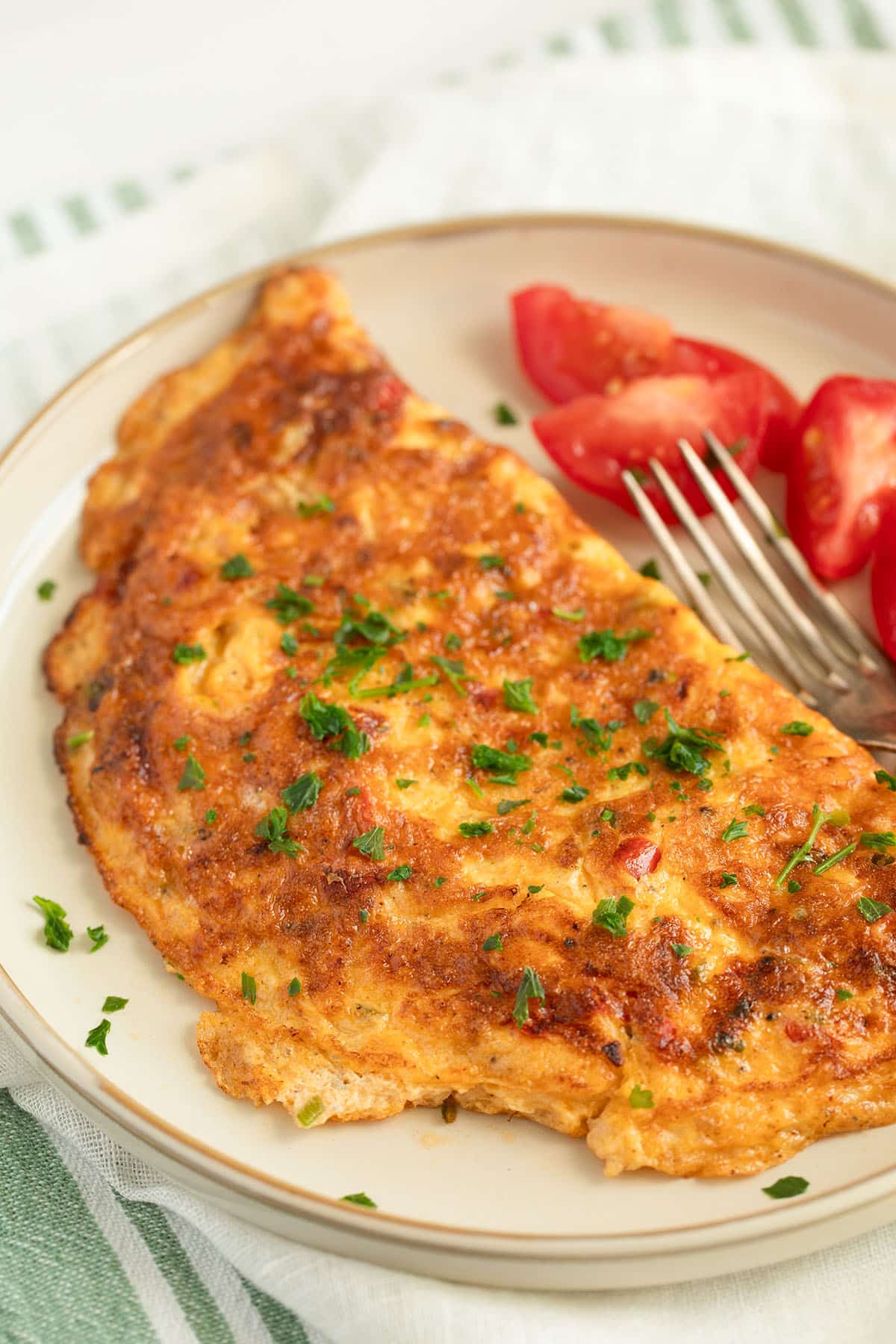 a chili omelette on a plate with small tomato wedges and a fork.