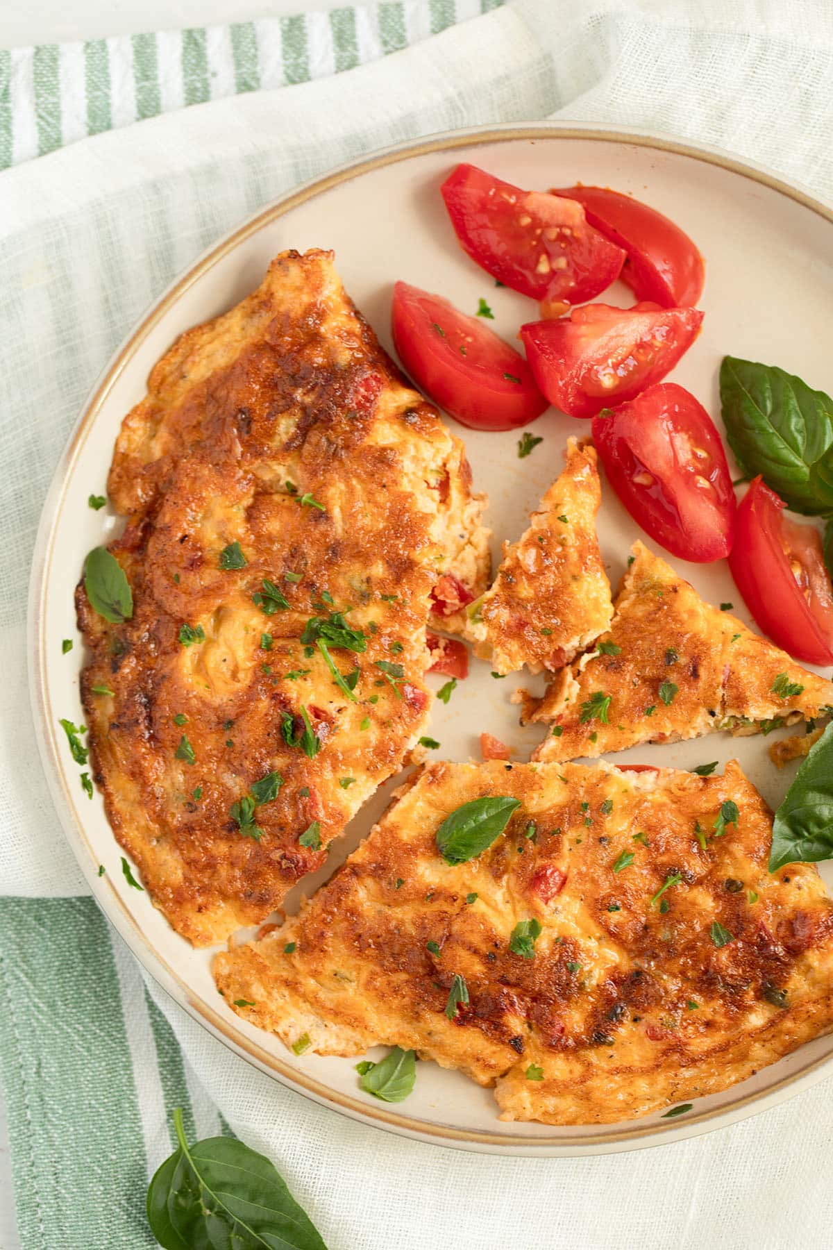 chili omelette served with tomatoes and basil leaves on a plate.